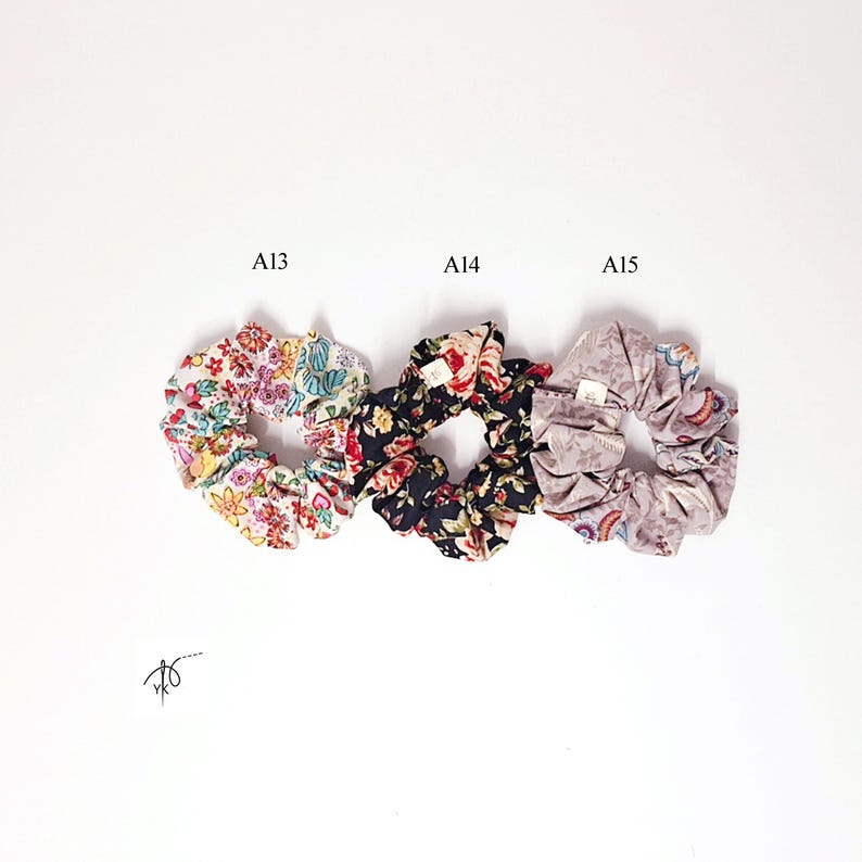 Pu&ograve; includere: Tre elastici per capelli floreali su sfondo bianco. Gli elastici sono etichettati A13, A14 e A15. A13 presenta un motivo floreale colorato, A14 ha un design floreale scuro e A15 mostra una stampa floreale tenue. Gli elastici sono in tessuto.