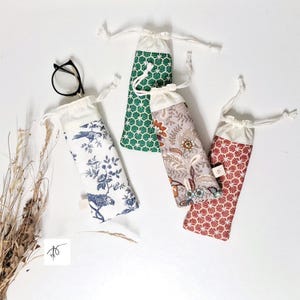 Peut inclure: Quatre pochettes rectangulaires en tissu avec fermetures à cordon. L'une présente un motif d'oiseaux et de fleurs bleu et blanc, une autre un motif géométrique vert, une autre un motif floral sur fond taupe, et une un motif géométrique rouge et blanc.