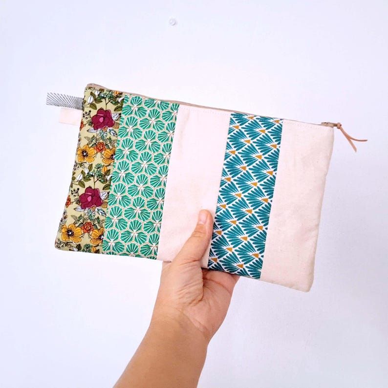 Op de afbeelding: Een rechthoekig etui met een beige achtergrond en kleurrijke panelen met patronen. De panelen hebben bloemen-, geometrische en waaiervormige ontwerpen in tinten groen, geel en blauwgroen. Een beige rits en een kleine stoffen lus zijn zichtbaar.