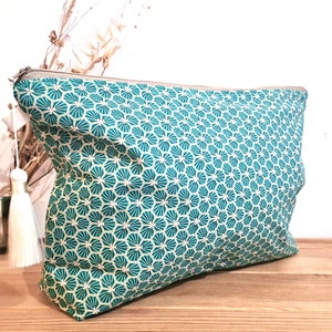 May include: A teal and white patterned zippered pouch with a white tassel. The pouch is made of fabric and has a geometric design.