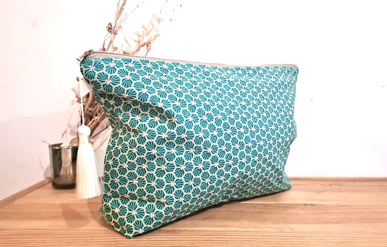 May include: A teal and white patterned zippered pouch with a white tassel. The pouch is made of fabric and has a geometric design.