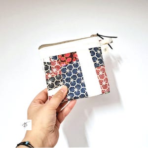 Puede incluir: Pequeño neceser cuadrado de patchwork con cierre de cremallera. El neceser presenta una mezcla de telas estampadas en rojo, azul marino y blanco. El diseño incluye patrones florales y geométricos. Un cordón negro y una pequeña etiqueta están unidos a la cremallera.