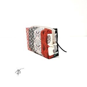 Peut inclure: Une pochette rectangulaire à fermeture éclair présentant un motif patchwork composé de divers dessins en forme d'éventail dans des tons de rouge, noir, blanc et gris. L'accessoire en tissu possède une fermeture latérale avec une tirette noire.