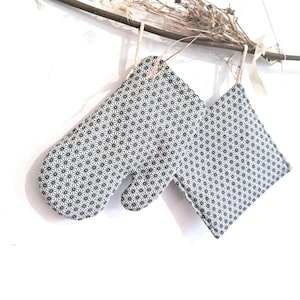 May include: A set of two black and white oven mitts with a geometric pattern. The mitts are hanging from a branch.
