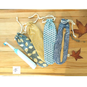May include: Four fabric drawstring pouches with varied patterns including ginkgo leaves, geometric stars, and ocean waves, alongside a white electric toothbrush and a wooden toothbrush, with a small white square logo featuring a needle and thread.