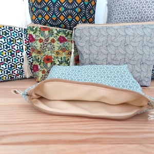 May include: A collection of fabric zipper pouches featuring various patterns including geometric shapes, floral prints, and abstract lines. Each pouch is equipped with a zipper closure and a small decorative tassel. One pouch is open, revealing a beige lining.