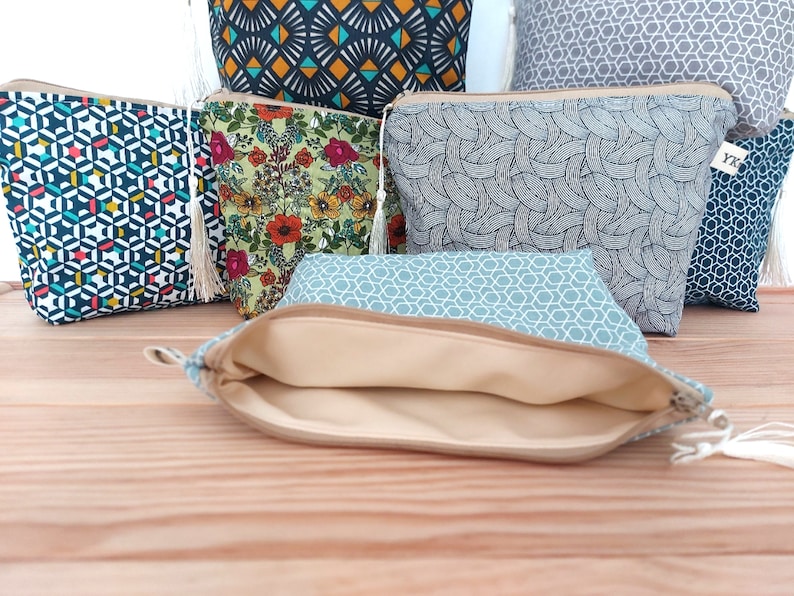 May include: A collection of fabric zipper pouches featuring various patterns including geometric shapes, floral prints, and abstract lines. Each pouch is equipped with a zipper closure and a small decorative tassel. One pouch is open, revealing a beige lining.