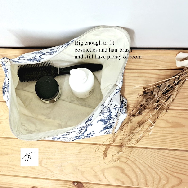 May include: A white zippered pouch with a blue floral pattern containing a black hairbrush, a black jar, and a white bottle. The interior text reads: Big enough to fit cosmetics and hair brush and still have plenty of room.