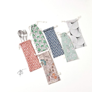 Può includere: Una collezione di sacchetti per posate riutilizzabili in vari modelli e colori, tra cui disegni rossi, verdi, blu e floreali. Ogni sacchetto ha una chiusura con coulisse e contiene un cucchiaio e una forchetta. I sacchetti sono disposti su una superficie bianca.