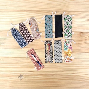 Puede incluir: Una colección de diez estuches rectangulares de tela para bolígrafos con varios patrones, incluyendo diseños florales, geométricos y negro sólido. Cada estuche tiene un cierre de cordón en la parte superior. Un estuche contiene dos bolígrafos y otro uno.