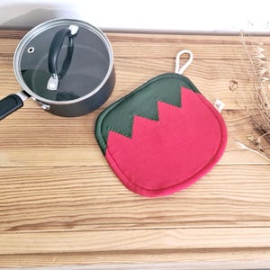 Könnte beinhalten: Ein roter und grüner Topflappen mit Zickzackmuster. Der Topflappen ist aus Stoff und hat eine Schlaufe zum Aufhängen.