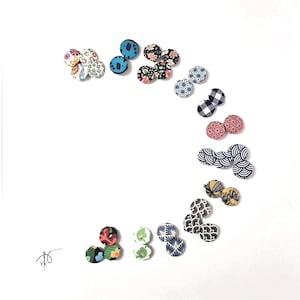 Può includere: Una collezione di bottoni rivestiti in tessuto con vari motivi e colori, tra cui floreali, geometrici e astratti. I bottoni sono disposti su uno sfondo bianco, mostrando le loro diverse trame e stili.