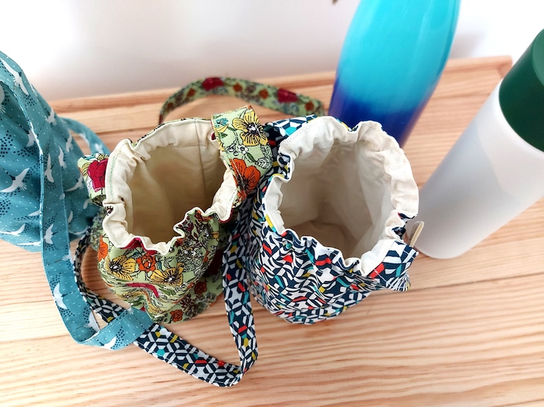 May include: Two small drawstring bags with floral and geometric patterns. One bag is green with orange and yellow flowers, the other is navy with a geometric design. Both have cream-colored interiors and matching straps.