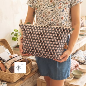 May include: A rectangular zippered pouch featuring a repeating black and pale pink fan-shaped pattern. The pouch has a cream-colored tassel attached to the gold-tone zipper pull. The fabric has a structured appearance with a visible side tag.