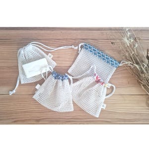 May include: Four white mesh laundry bags with drawstring closures. Two bags have blue and white patterned trim, one has red and white patterned trim, and one has a white bar of soap inside.