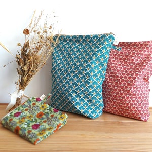 May include: Three fabric pouches in teal, red, and floral patterns. The teal pouch has a geometric design with gold accents. The red pouch features a repeating shell-like pattern. A small floral pouch is also present.