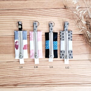 May include: Four small rectangular fabric pouches with zippers and key rings. The pouches feature various patterns, including floral, polka dots, and geometric designs. Each pouch has a silver zipper and a small fabric loop at the bottom. The pouches are labeled L9, L10, L11, and L12.