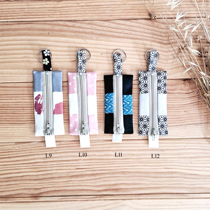 May include: Four small rectangular fabric pouches with zippers and key rings. The pouches feature various patterns, including floral, polka dots, and geometric designs. Each pouch has a silver zipper and a small fabric loop at the bottom. The pouches are labeled L9, L10, L11, and L12.