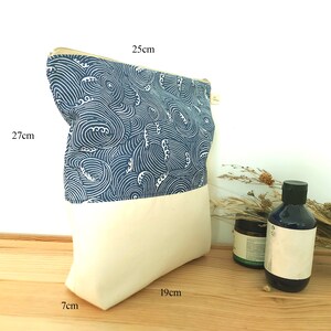 May include: A rectangular pouch with a cream-colored bottom and a blue and white wave pattern top. The pouch is 10.6 inches tall, 9.8 inches wide, and 2.8 inches deep. A gold zipper runs along the top. The pouch is on a wooden surface.