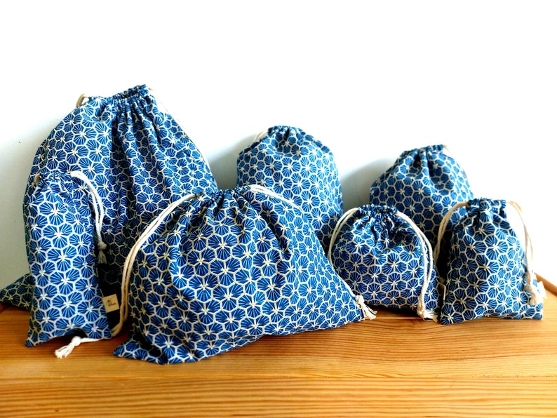 Pode incluir: Conjunto de sete sacos de cord&atilde;o azul e branco com um padr&atilde;o geom&eacute;trico. Os sacos s&atilde;o feitos de tecido e t&ecirc;m um fecho de cord&atilde;o.