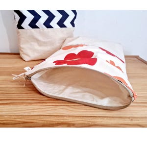 May include: Open canvas zipper pouch with a floral pattern in red and orange. A second canvas bag with a navy and white chevron pattern is in the background. Both bags are on a wooden surface.