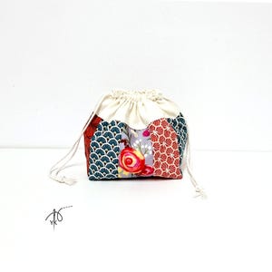 Peut inclure: Une petite pochette à cordon avec un design en patchwork composé de panneaux à motifs d'éventails bleu foncé et rouge, ainsi qu'une section centrale à imprimé floral de roses rouges et jaunes sur fond gris clair, terminée par un haut crème.