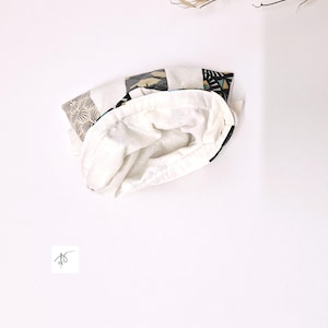 Op de afbeelding: Een witte stoffen tas met een patroon aan de buitenkant. De buitenkant heeft geometrische en abstracte ontwerpen in zwart, grijs en beige. De binnenkant is effen witte stof. De tas is open en onthult de witte binnenkant.