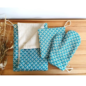 Op de afbeelding: Een set van drie keukentextiel met een teal en gouden geometrisch patroon. De set bevat een ovenwant, een theedoek en een wafeldoek.