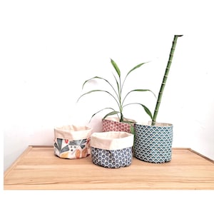 Może przedstawiać: Cztery kosze do przechowywania z tkaniny z różnymi wzorami. Kosze znajdują się na drewnianej powierzchni. Kosze są w następujących kolorach: czerwony, niebieski, biały i zielony.