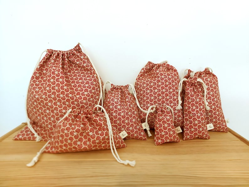 May include: Set of seven red and white drawstring bags with a floral pattern. The bags are arranged in size order from largest to smallest.