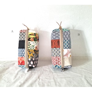 Op de afbeelding: Twee rechthoekige patchwork stoffen zakjes met ritssluitingen. De zakjes zijn gemaakt van diverse stoffen met patronen in kleuren als rood, blauw, zwart en wit. Elk zakje heeft een leren koordlus aan de bovenkant.