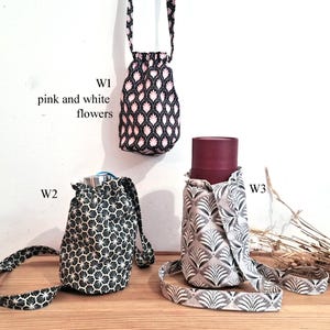 May include: Three fabric water bottle holders in different patterns. One is black with pink and white flowers, another is black and white geometric, and the third is gray and white with a leaf design. Each has a strap.