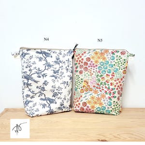 May include: Two fabric pouches with zipper closures. One pouch features a blue and white bird and floral pattern. The other pouch has a colorful floral design with pink, yellow, and green hues. The pouches are on a wooden surface.