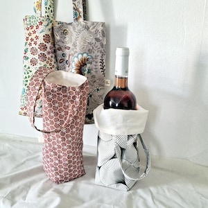 May include: A collection of fabric wine bottle bags and tote bags. The bags display diverse patterns, including floral and geometric designs. One bag contains a wine bottle. The bags are designed for carrying wine bottles.