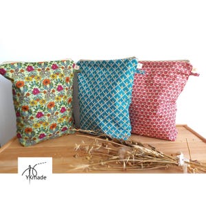 May include: Three fabric pouches with zipper closures. One pouch has a floral pattern with orange, pink, and yellow flowers on a green background. Another is teal with a geometric design. The third is red with a repeating pattern.