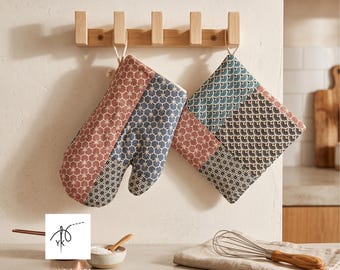 Puede incluir: Un guante de cocina acolchado y un agarrador cuadrado con un diseño de patchwork de patrones geométricos de abanicos y estrellas en tonos terracota, azul marino y negro. Ambos artículos incluyen una trabilla de tela para colgar.