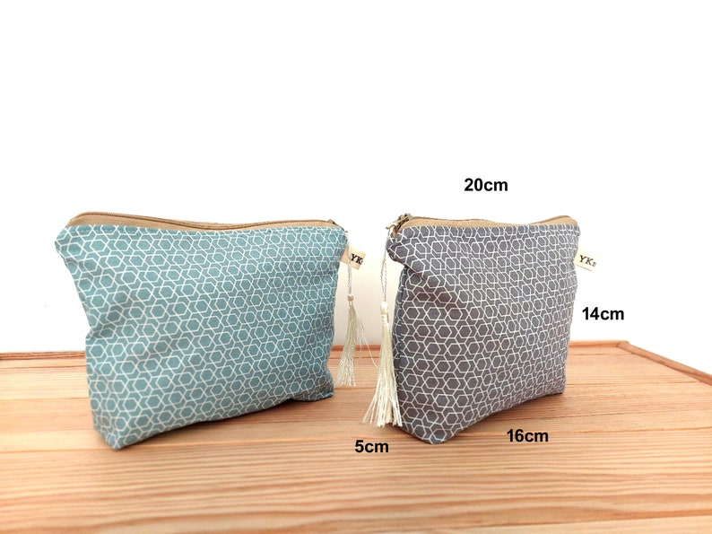 May include: Two zippered pouches featuring a geometric star pattern. One pouch is teal and the other is gray. Each has a beige zipper and a small white tassel. The gray pouch is labeled with dimensions of 20cm by 14cm by 5cm, which is approximately 7.9in by 5.5in by 2in.