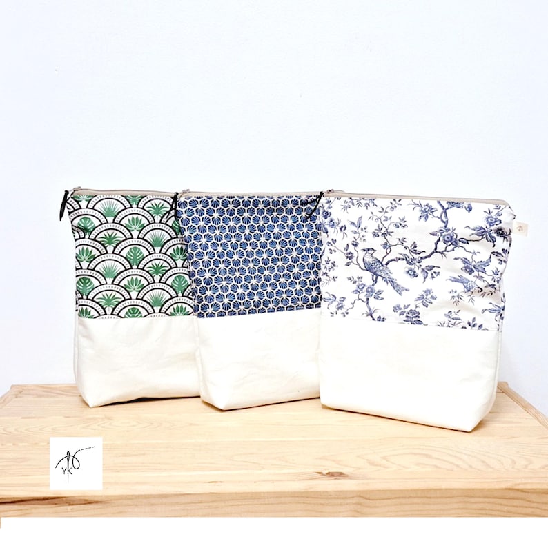 May include: Three fabric pouches with zipper closures. The pouches have a white base and are topped with patterned fabric in green, blue, and white. The patterns include a fan design, a geometric pattern, and a floral bird design. The pouches are on a wooden surface.