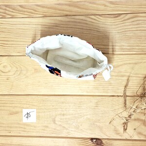 May include: A drawstring pouch, open to reveal a white interior. The exterior is patterned with blue, red, and black floral designs. The pouch rests on a light brown wooden surface.