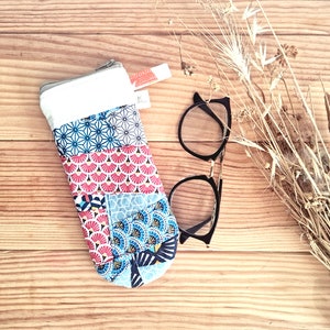 Può includere: Un astuccio per occhiali in tessuto con motivo colorato e chiusura a zip. L'astuccio è appoggiato su una superficie di legno accanto a un paio di occhiali neri.