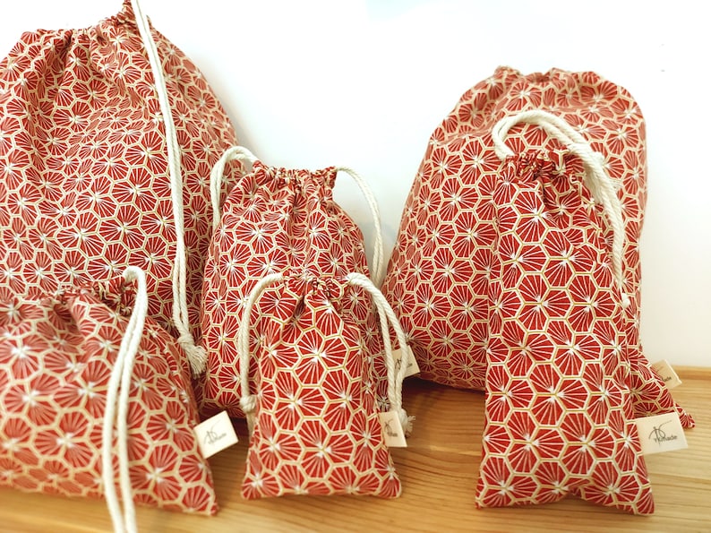 May include: Set of five red and white drawstring bags with a geometric pattern. The bags are made of fabric and have a white drawstring closure. The bags are arranged in a row from largest to smallest.