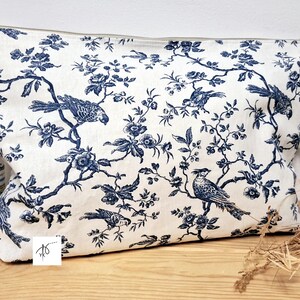 May include: A rectangular zippered pouch featuring a white fabric base with a dark blue toile pattern. The design displays intricate illustrations of various birds perched on flowering branches with leaves and blossoms across the entire surface.
