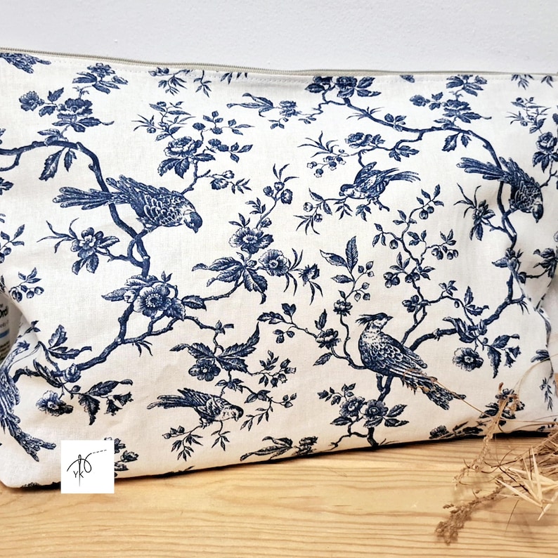 May include: A rectangular zippered pouch featuring a white fabric base with a dark blue toile pattern. The design displays intricate illustrations of various birds perched on flowering branches with leaves and blossoms across the entire surface.
