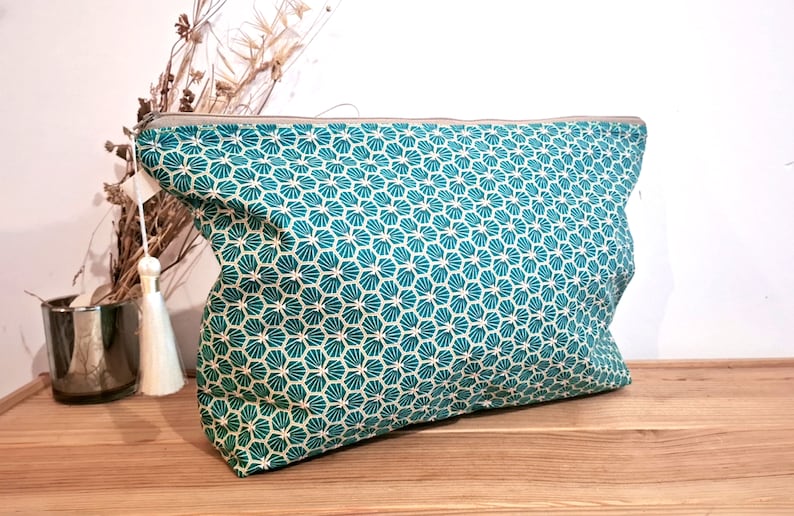 May include: A teal zippered pouch with a white and teal geometric pattern. The pouch has a white tassel.