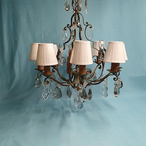 May include: A six-light chandelier with a gold metal frame and clear crystal drops. The chandelier has white fabric lampshades.