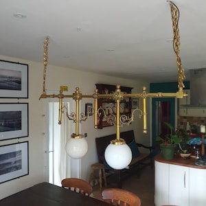 May include: A vintage brass chandelier with two white globe lights. The fixture has ornate detailing and is suspended from the ceiling by brass chains. The design includes decorative elements and a small plate with the text "DY 566".
