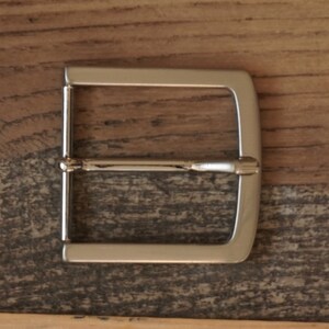 May include: A silver metal belt buckle with a rectangular shape and a smooth finish.