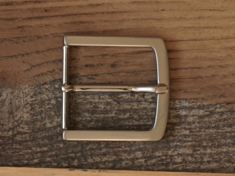 May include: A silver metal belt buckle with a rectangular shape and a smooth finish.