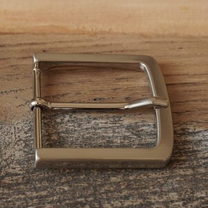 May include: A silver metal belt buckle with a smooth, polished finish.