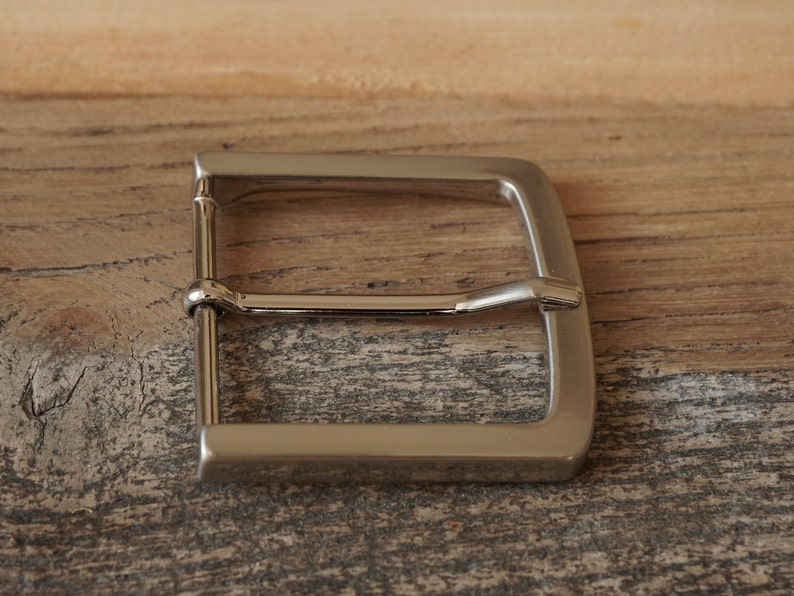 May include: A silver metal belt buckle with a smooth, polished finish.